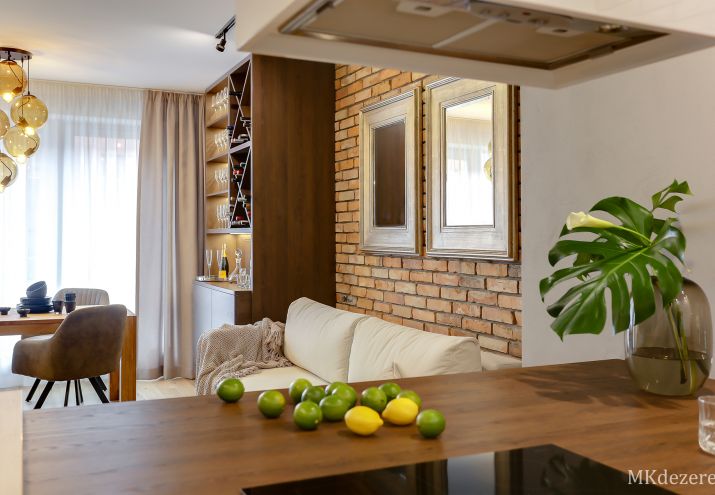 W salonie nad kanapą na tle ceglanej ściany zostały zawieszone lustra w złotych ramach.