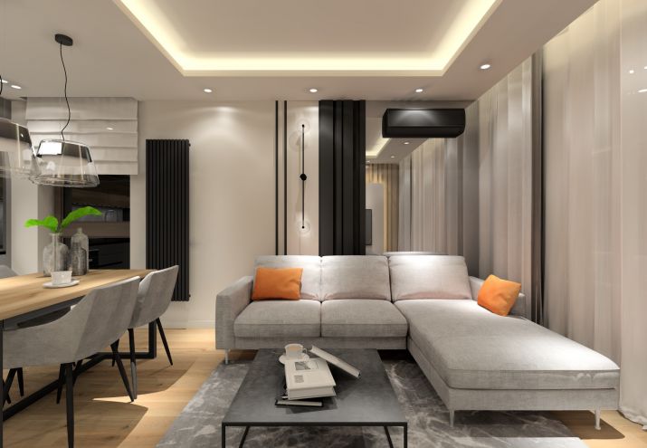 Szary narożnik w małym salonie, akcentem kolorystycznym są pomarańczowe poduszki.