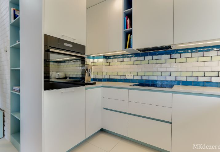 Białe płytki w kuchni na podłodze i na ścianie w połączeniu z niebieskimi i zielonymi płytkami.