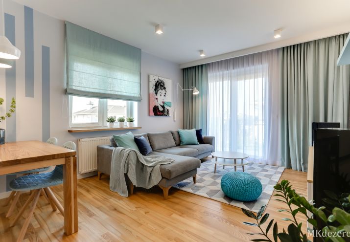 Projekt salonu z szarym narożnikiem, niebieskimi i zielonymi dodatkami.