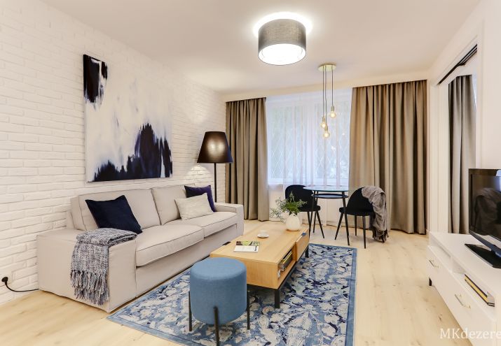 Salon z białą cegłą, nad kanapą wisi duży obraz abstrakcyjny kolorystycznie nawiązujący do dywanu.