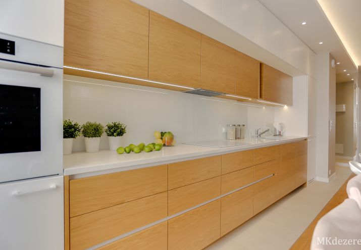 Aranżacja białej kuchni z elementami drewna i kamiennym białym blatem.