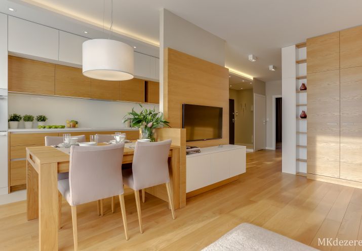 Stół oddzielający kuchnię od salonu. Na ścianie wiszący telewizor.